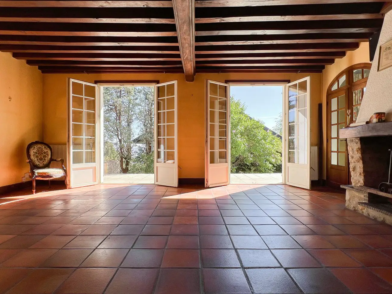 Grande pièce à tomettes et poutres apparentes ouverte sur le jardin