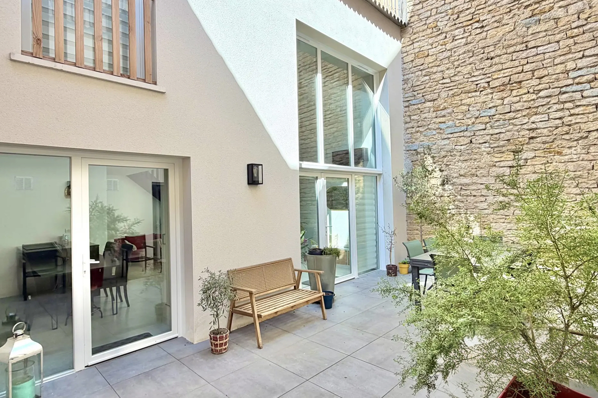 Patio pavé avec banc en bois entre un mur en pierre et une façade claire