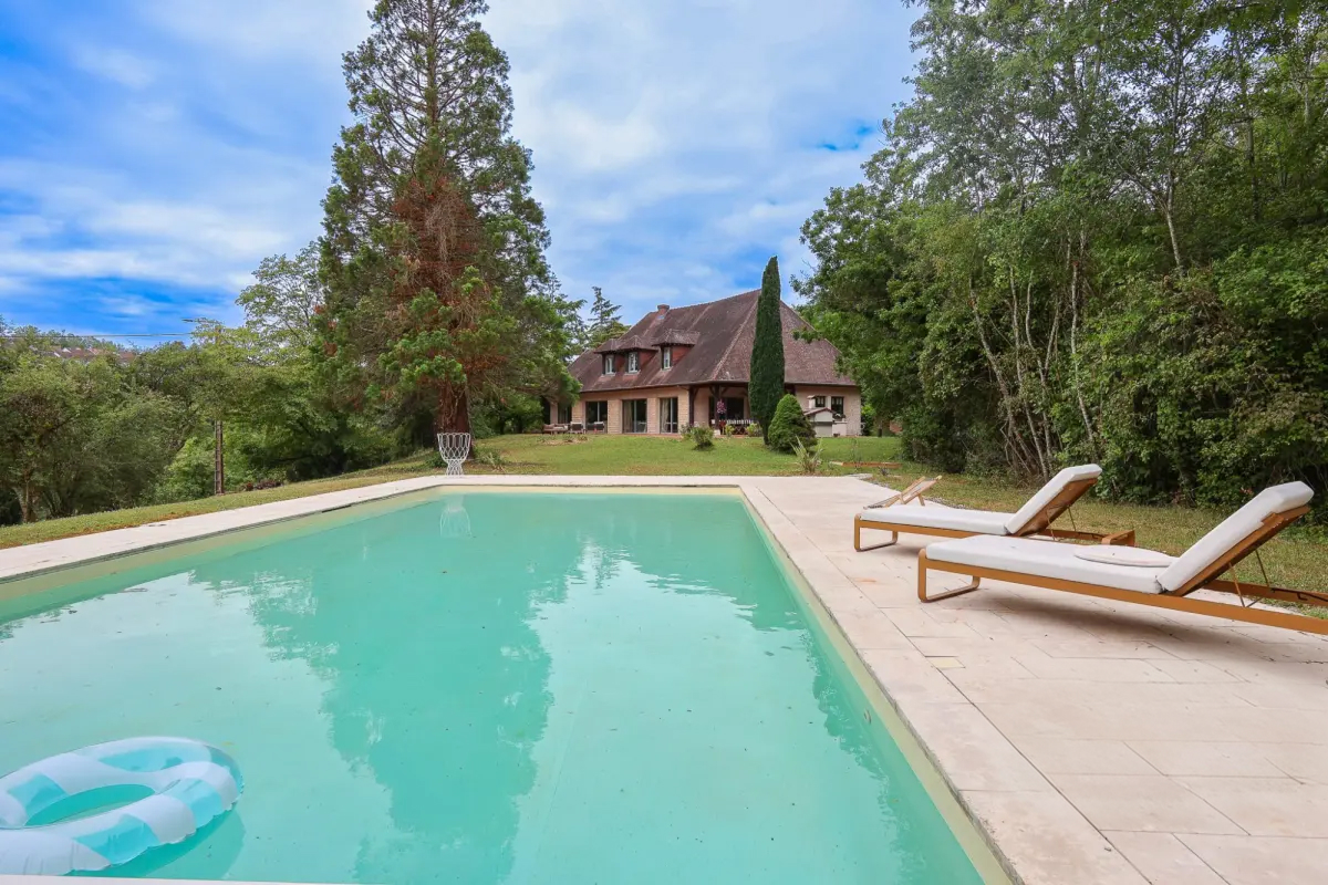 Piscine et transats devant une maison entourée d'arbres