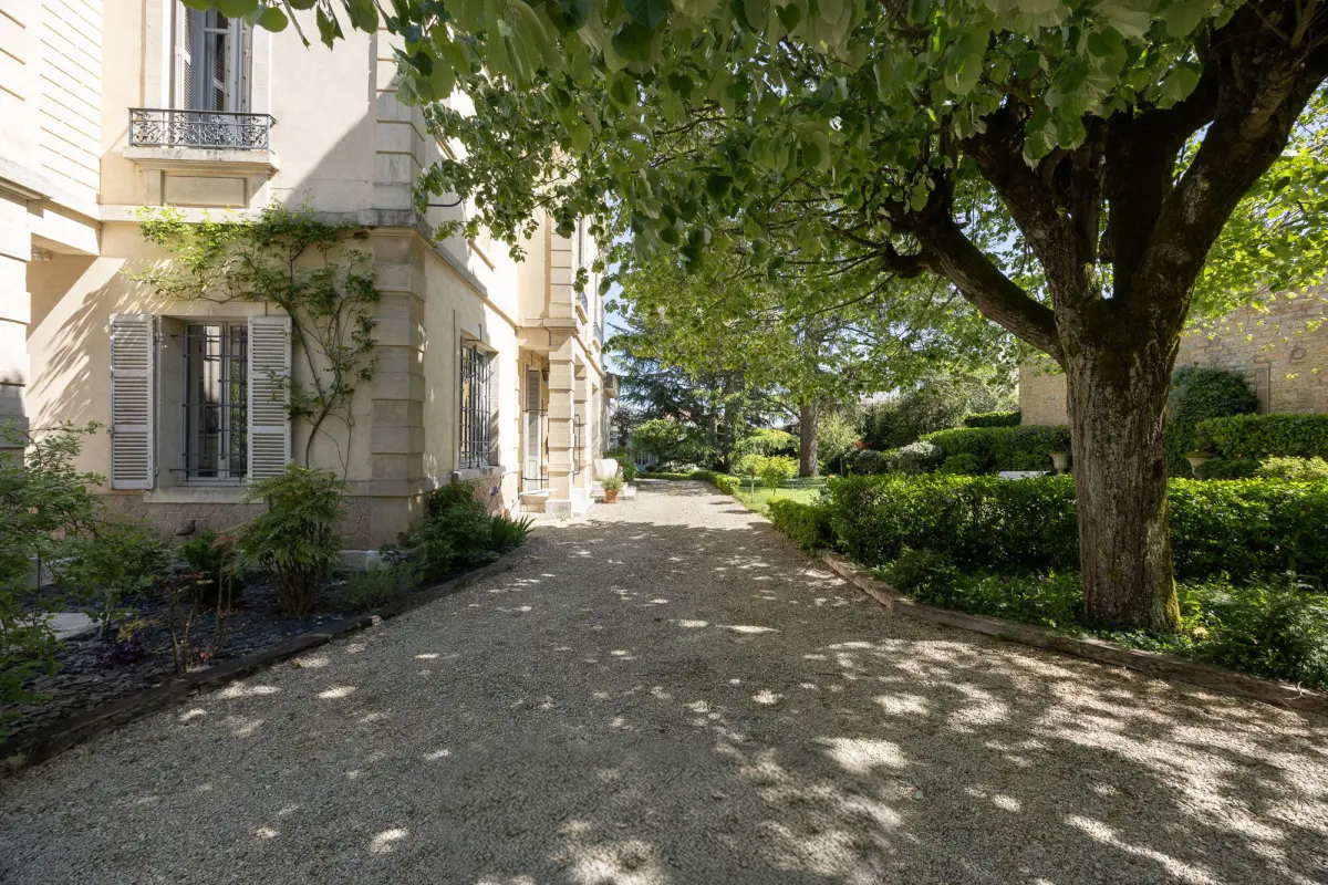 Allée de gravier bordée d'arbres devant un hôtel particulier