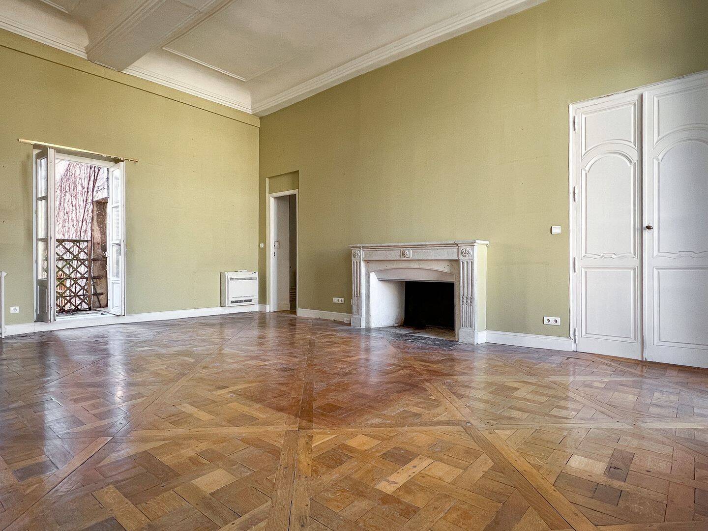 Grand salon aux murs vert olive avec cheminée de marbre et parquet en point de Hongrie