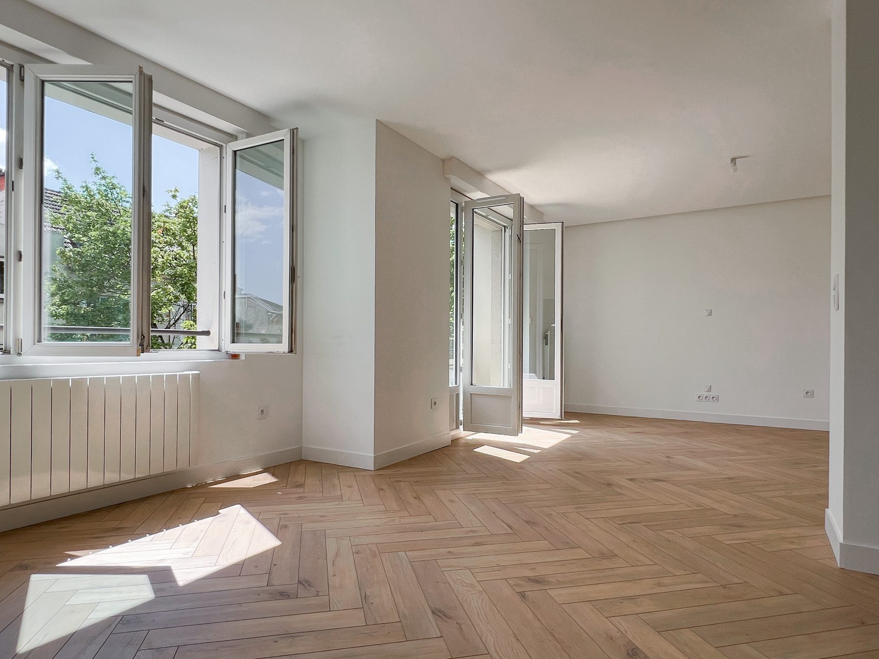Séjour lumineux à parquet à chevrons et fenêtres ouvertes sur les toits de Dijon