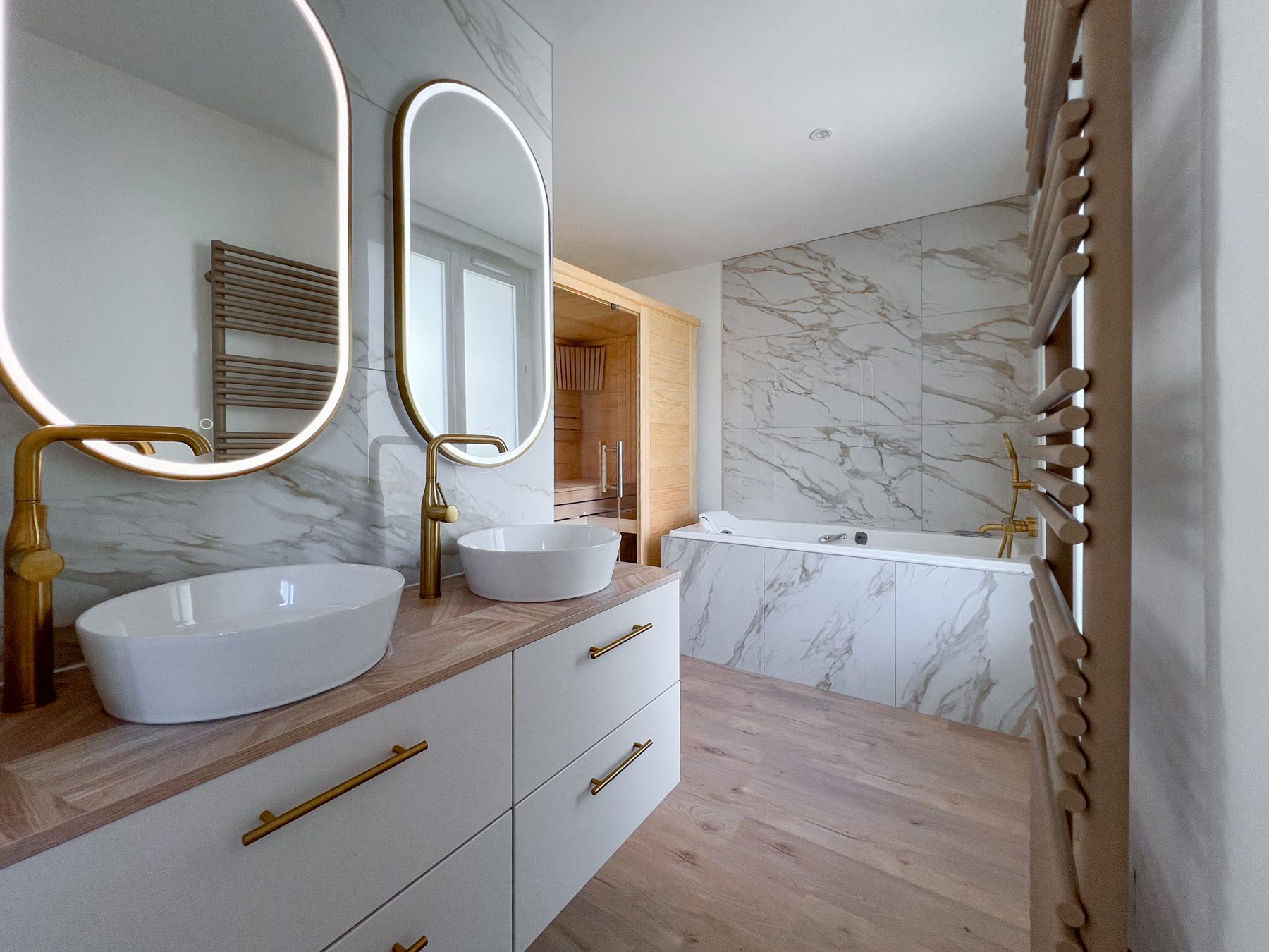 Salle de bains en marbre veiné avec double vasque, miroirs ovales et robinetterie dorée