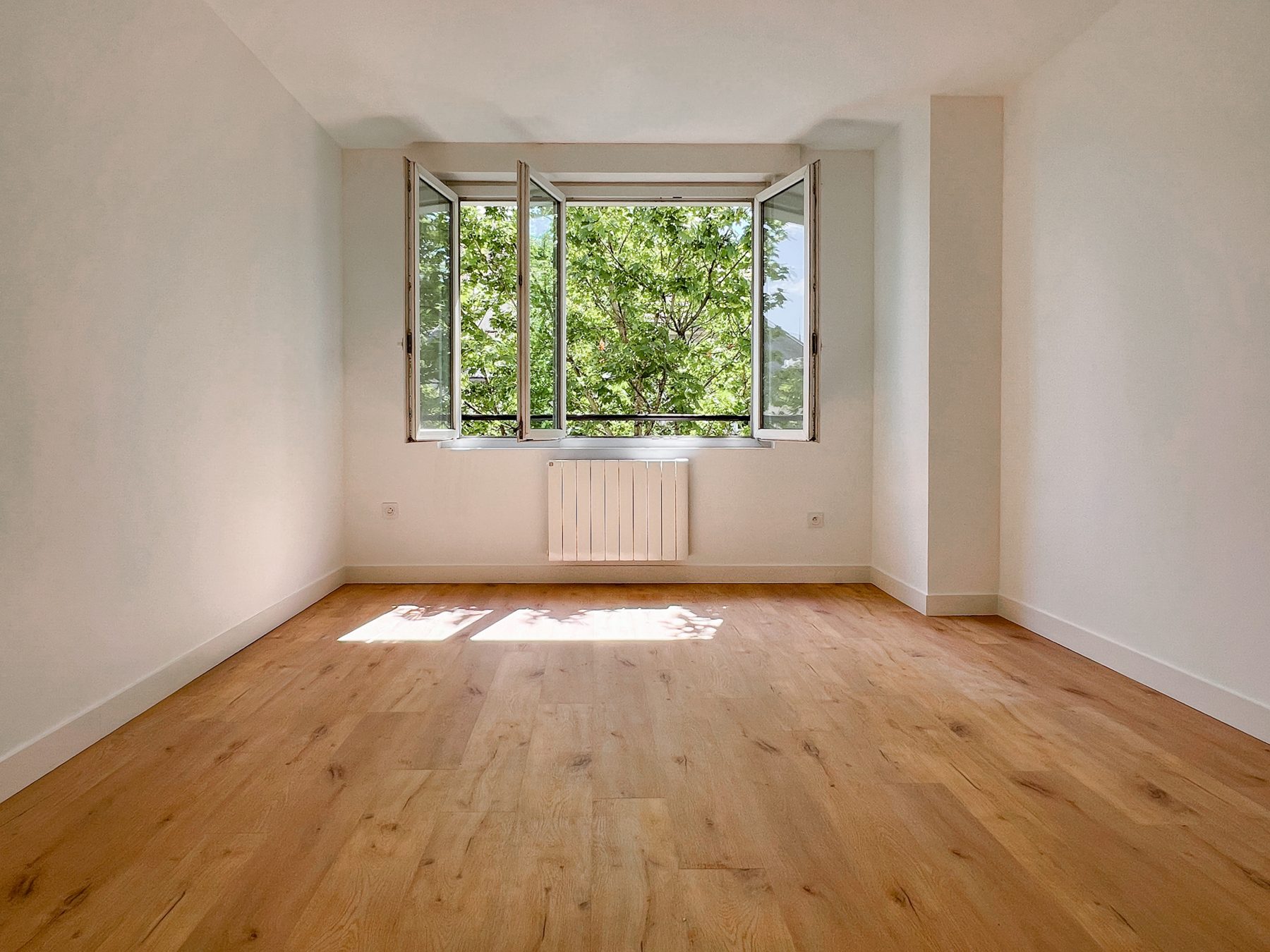 Chambre au parquet clair ouverte sur la verdure de la cour